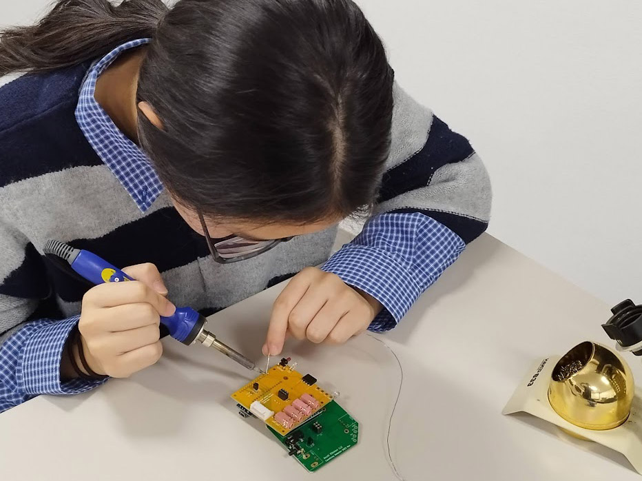 参加メンバーがひとり、白いテーブルでPCBにはんだごてを当てている真上からの一枚