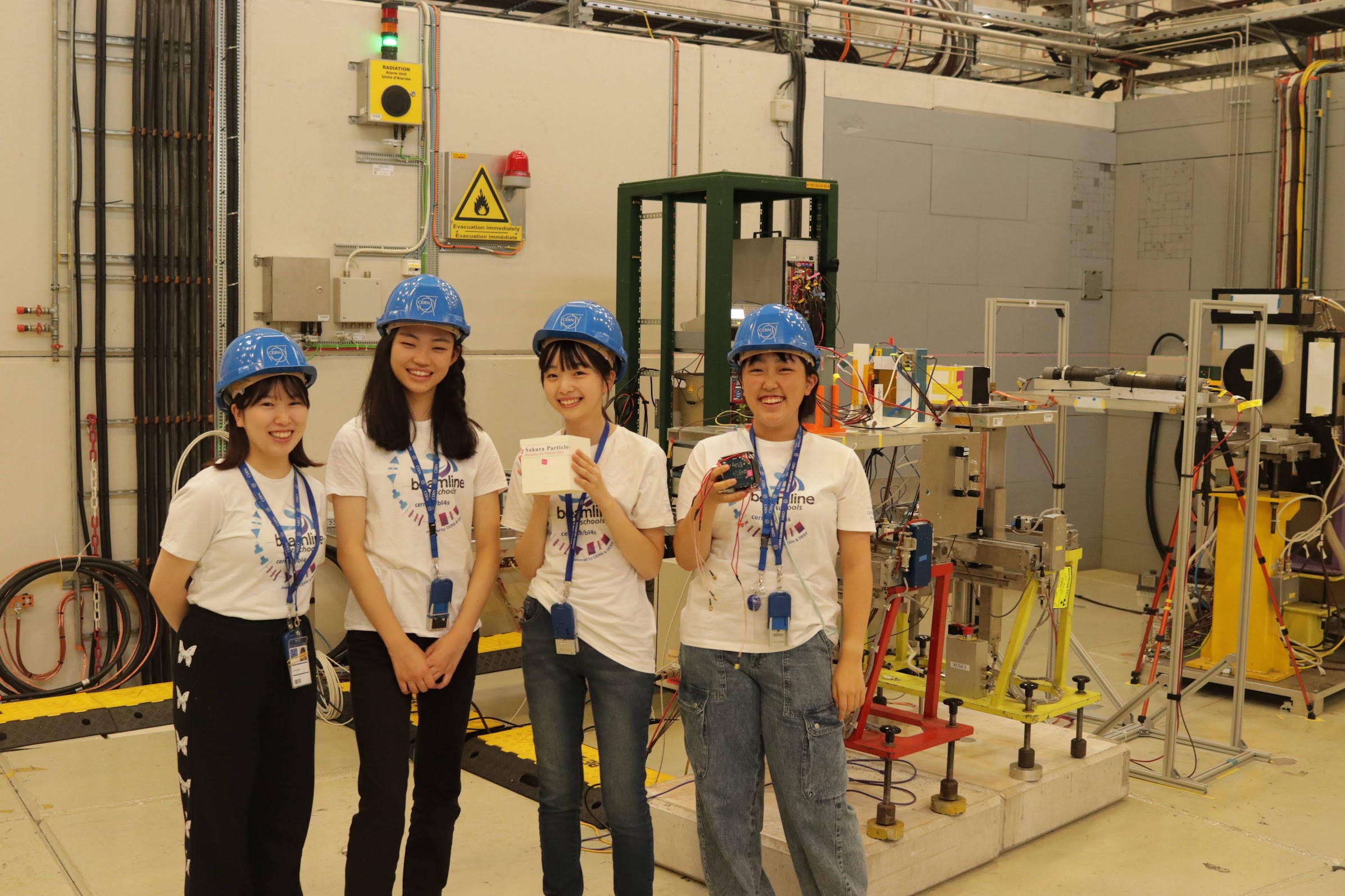 CERN Beam Line for Schools の実験エリアで、ヘルメット姿の女子4人組チーム Sakura Particles が並ぶ