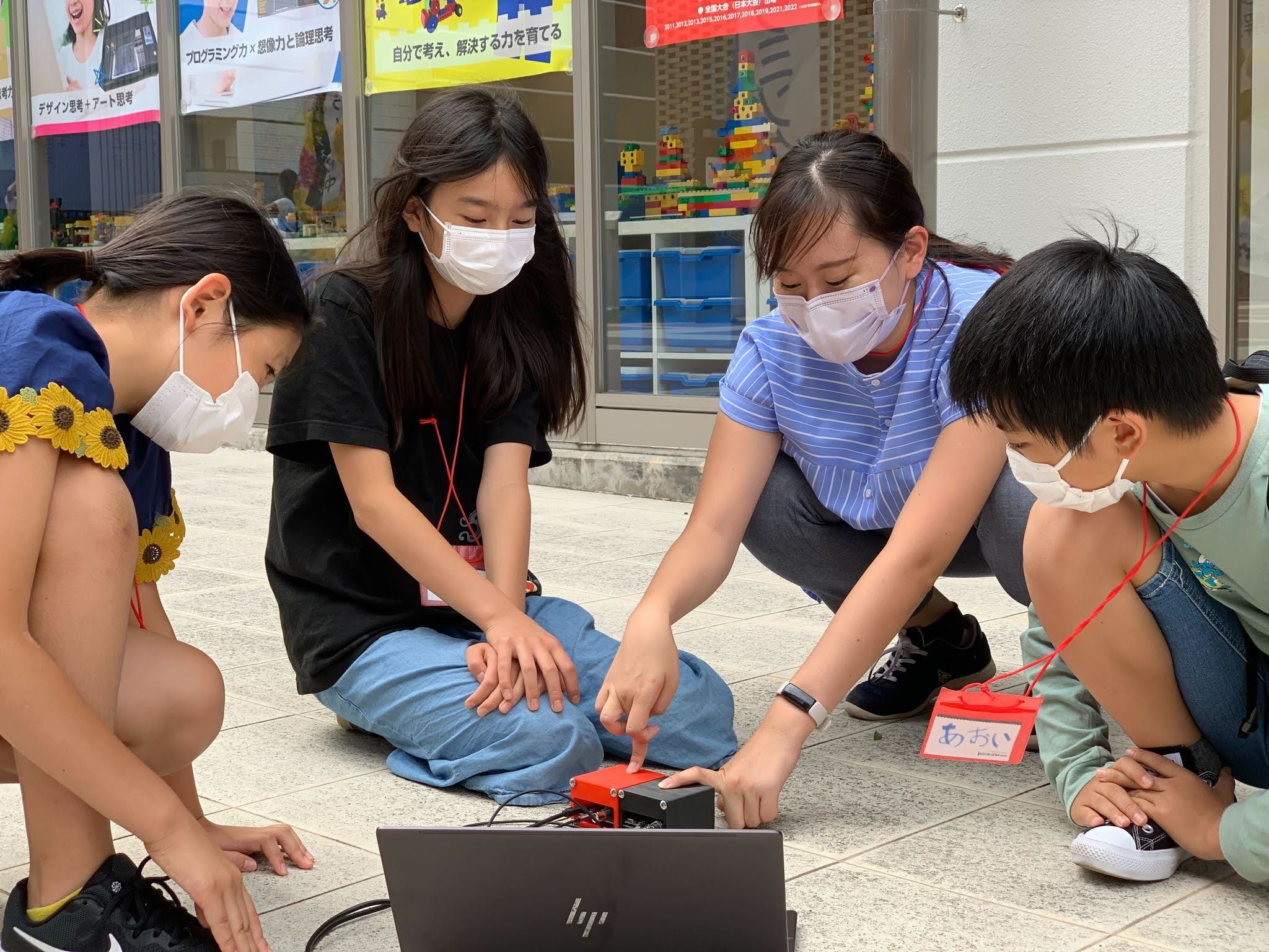 屋外でしゃがみこみ、ノートPCと検出器を見ながら測定する中学生たちとメンター