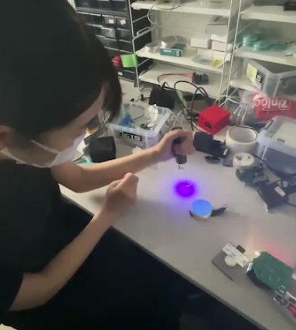 実験室の机の上で、青く光る自作シンチレータを生徒がのぞき込んでいる様子