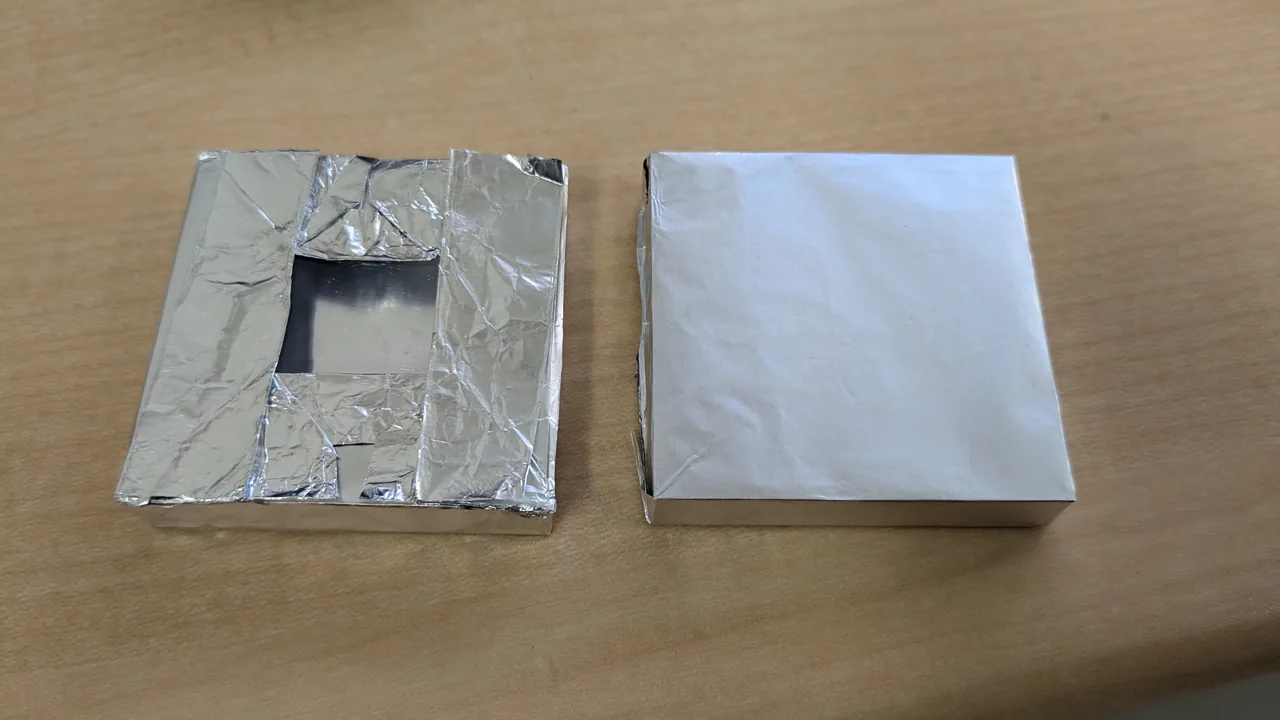 Two scintillators wrapped in aluminum foil. The one on the left has a square window in the middle of one face