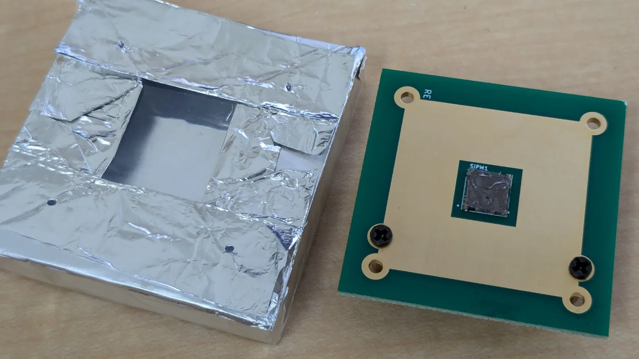 A scintillator with a window open next to a SiPM board. The SiPM's light-receiving surface is visible