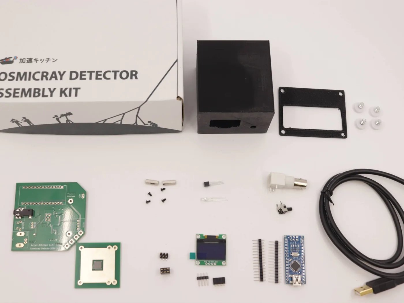 The contents of the assembly kit: a black case, boards, an OLED, an Arduino Nano, pin headers, a USB cable and more, with COSMICRAY DETECTOR ASSEMBLY KIT printed on the box