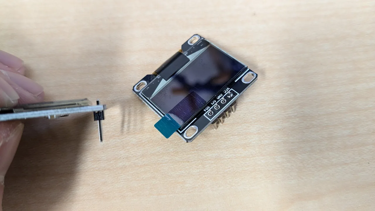 A hand holding the pins upright against the board, and an OLED module