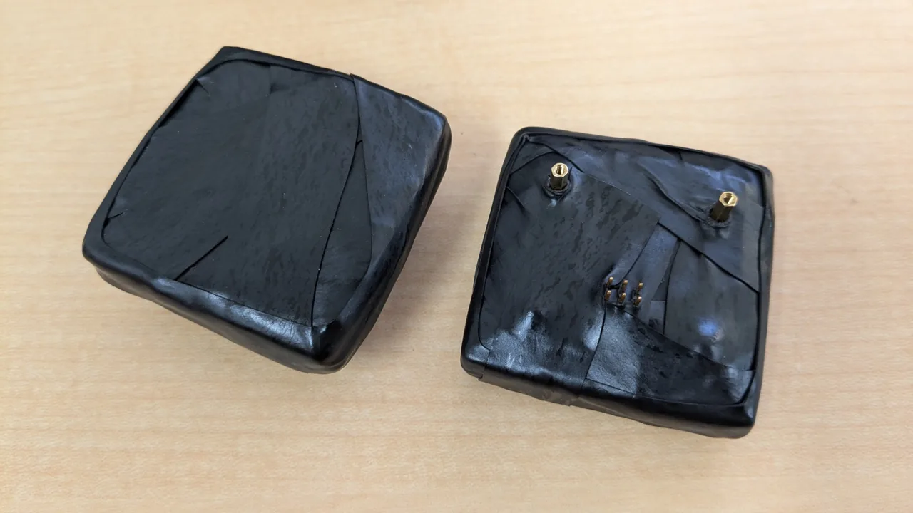 A scintillator block wound in black light-shielding tape, and a SiPM board with its spacers and terminals sticking out