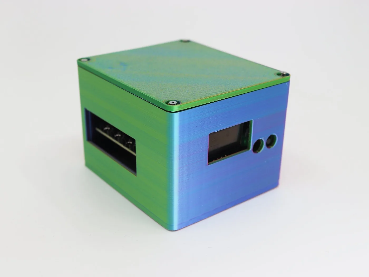 The v2 (OHASHI) case: a nearly cubic box with a window for the display and two round holes on a side face, and a green lid