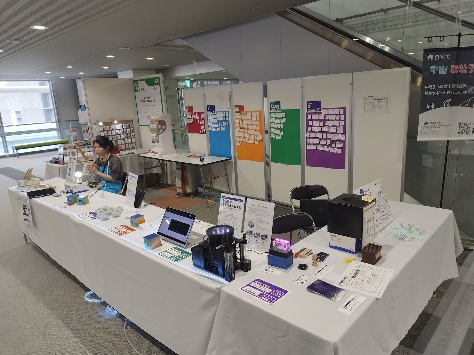 The whole booth: five devices on a white table, with five coloured boards on the wall behind