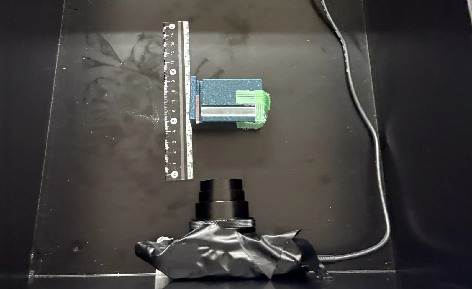 Top view inside the light-tight box: a silver CsI scintillator on a blue stand beside a ruler, with the lens of the cooled camera below it